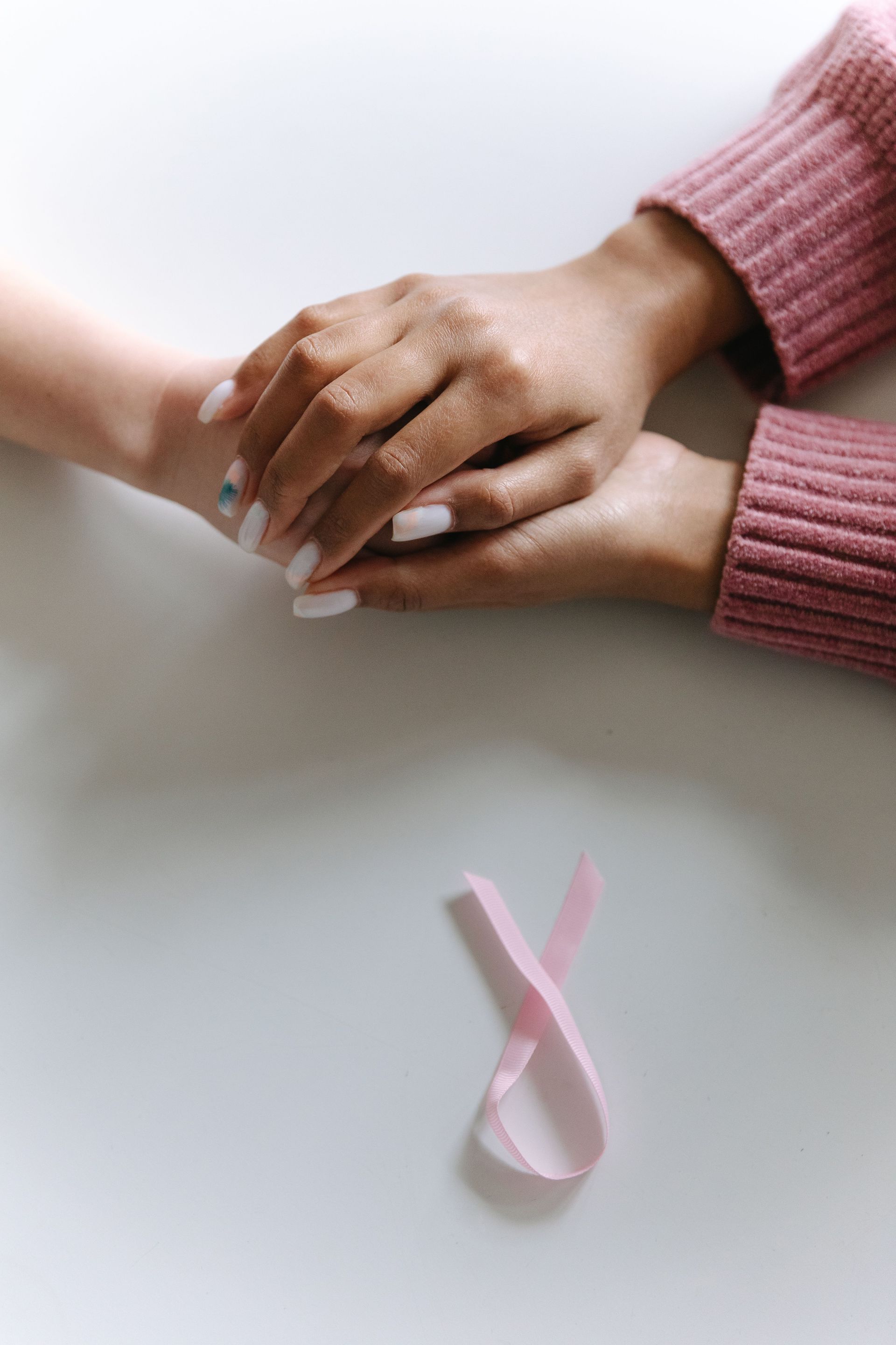 Close-up of two hands holding with a pink ribbon symbolizing cancer awareness.